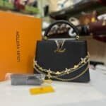 Black structured top-handle bag with floral chains and matching strap
